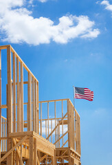 American flag waving in the wind on the top of a construction home framing. Blue sky and white clouds background.