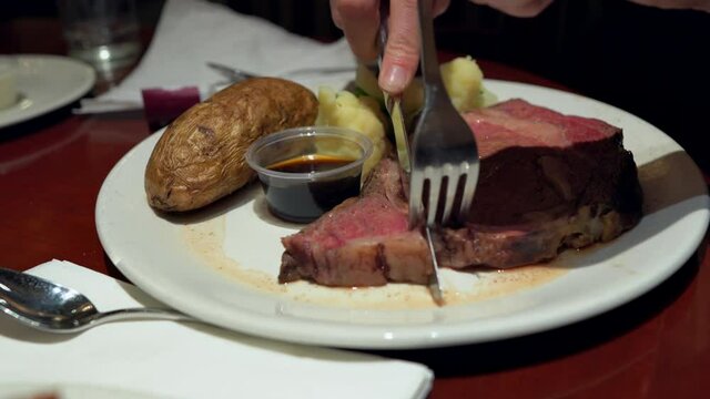 This close up video shows anonymous hands cutting into a juicy prime rib dinner meal at a restaurant.