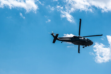 Military helicopter flying over bright blue skies with fluffy white clouds.