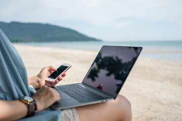 Woman using laptop and smartphone to work study in vacation cady at beach background.