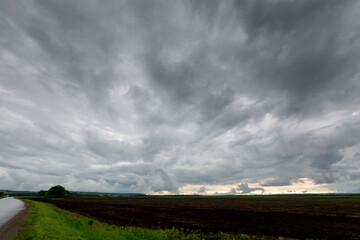 Stormy sky with fresh arable land and road in the corner