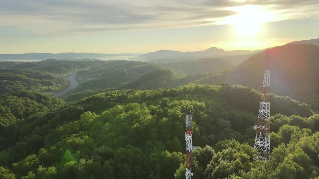Aerial view of 4G and 5G Telecom Tower on the top of hill covered of green forest during golden hour