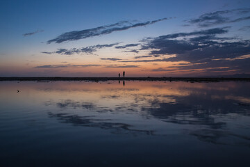 sunset on Central California beach with human silhouettes reflecting in water