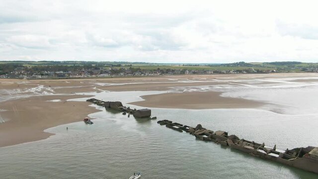 Mulberry sandy beach with ruins of WWII fortification washed by sea water on a cloudy day in France
