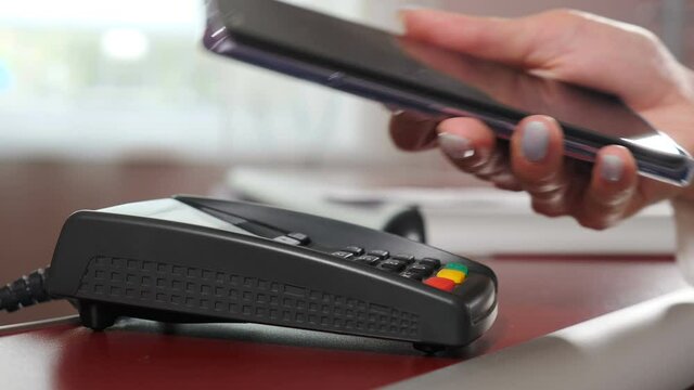 Mobile payment. Contactless payment with your smartphone. Wireless payment concept. Close-up, woman using smartphone cashless wallet NFC technology to pay order on bank terminal. 4 k video