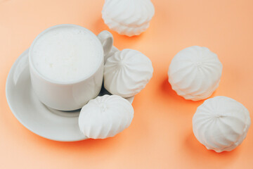 Cup of cappuccino and white marshmallows on orange background close up