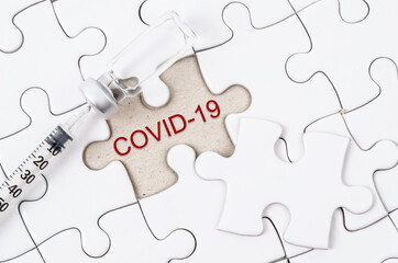 Fototapeta premium Vaccine and syringe injection with COVID-19 text on jigsaw.