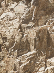 Natural background. Closeup edged shabby cliff cracks. Gray-brown stone rock texture of mountains. Vintage and faded matt style colour in tinted photo. Concept of geolog, mountaineering or hard work