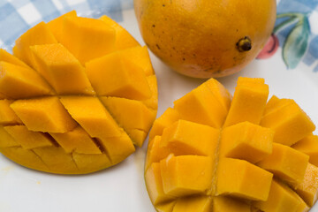 Sliced and ripe mangoes with an uncut mango on a white plate showing off the bring orange of ripeness