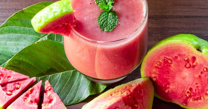 Glass of red guava juice and sliced guava slice on wooden background