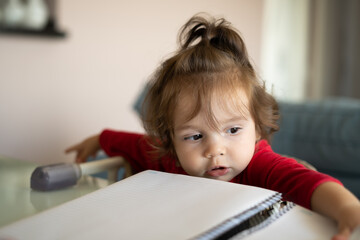 Bebe sentada na cadeirinha próxima a mesa e brincando com um caderno