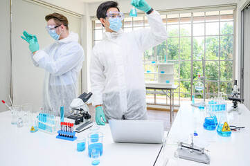 Couple male scientist wearing protection suit holding vaccine and working with many lab equipment for research vaccine at laboratory.