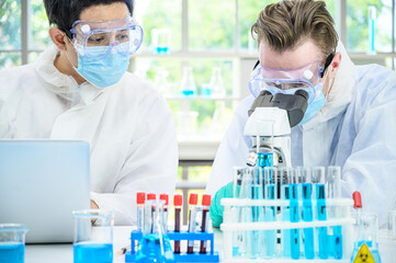 Couple male scientist wearing protection suit working with many lab equipment and computer laptop  for research vaccine at laboratory.