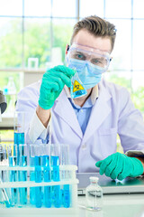 Lab equipment with blue liquid inside stand on the table with male scientist wearing protection suit holding beaker or tube with sample liquid inside for research at laboratory at the background.