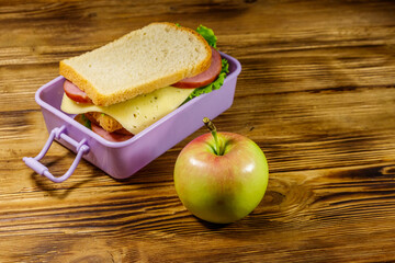 Lunch box with sandwiches and apple on a wooden table