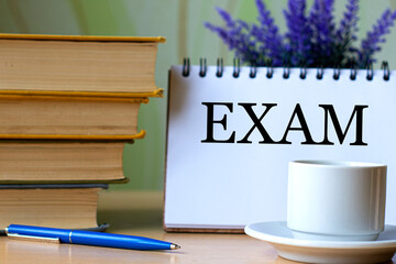 EXAM - word in a notebook on a background of old books with pen and white cup