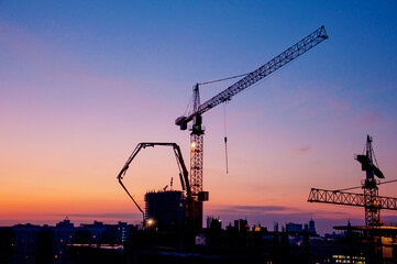 Industrial construction cranes and building silhouettes at sunrise or sunset. Urban city development.