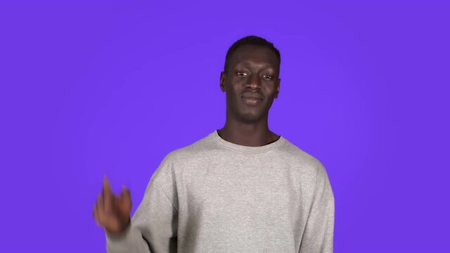 Say hello A friendly smiling black man waves affably at the camera. Standing over blue background and waving hi gesture