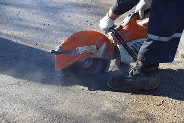 Close-up of a worker with a circular saw sawing asphalt, Parking construction.
