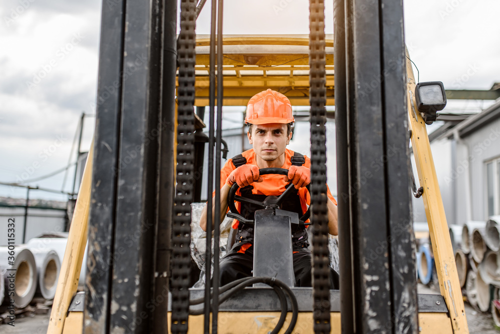 Wall mural front view of a serious face young caucasian man builder in overalls and orange protective helmet dr