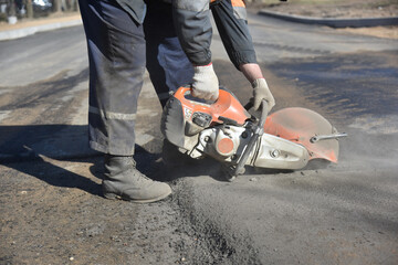 Obraz premium Pracownik w kombinezonie tnie asfalt piłą tarczową, budowa autostrady.