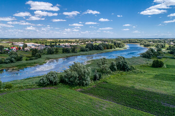 Fototapeta na wymiar A small river flowing through meadows and agricultural fields. Aerial view. Evening shot with the setting sun.