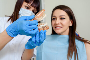 woman dentist explain to the patient on a tooth maxillary model the position of the future implants