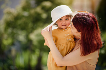 Portrait of a young happy beautiful mother with her little smiling daughter wearing a funny oversize white hat on green blurred background