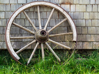 Old wooden rural cart wheel symbolizing the past on green grass against wooden background