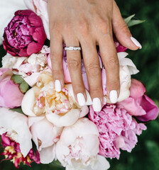 Fototapeta premium bride's hand with an elegant wedding ring with white gold diamonds on a bouquet of their peonies