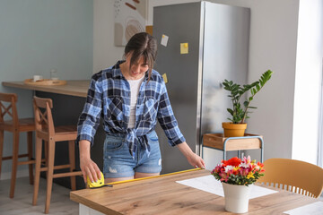Young woman measuring table in kitchen