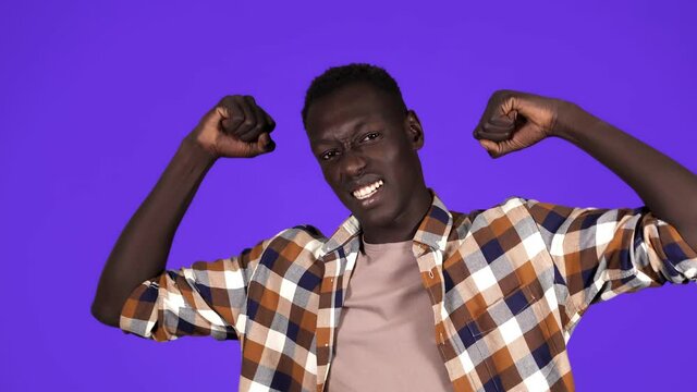 Strong afro american young man wearing plain shirt isolated on blue background in studio showing muscules at camera, sportsman. People sincere emotions, lifestyle concept