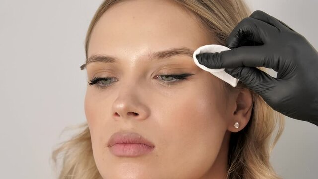 Professional master eyebrow woman removes liquid on the eyebrows with a cotton swab in a beauty salon. Permanent makeup for eyebrows. Eyebrow lamination and styling