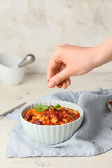 Woman sprinkling spices onto tasty pasta and beans in bowl on table