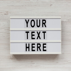 'Your text here' words on a lightbox on a white wooden surface, top view. Flat lay, overhead.