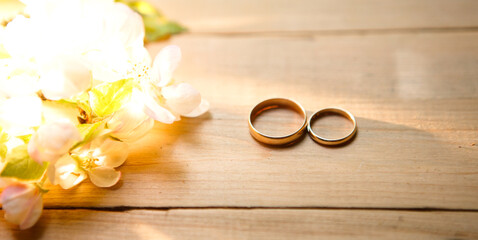 Two gold rings on a wooden background with white Apple blossoms. Wedding in eco-style, rustic. Couple in love, ceremony and registration, details, bride's fees, groom's morning. Space for text. flatly