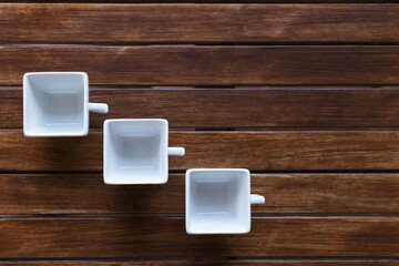 overhead view of three square white cups with handle facing right on brown wood laminate table