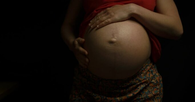 Young pregnant woman showing and feeling her baby bump under her shirt