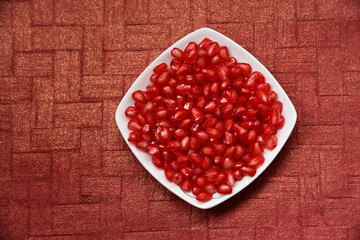 pomegranate seeds in a dish with textured background.