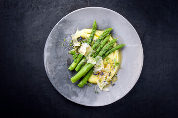 Traditioneler gedämpter grüner Spargel mit Kartoffel Püree Creme und Parmesan Käse angeboten als Draufsicht auf einem Modern Design Teller mit Textfreiraum