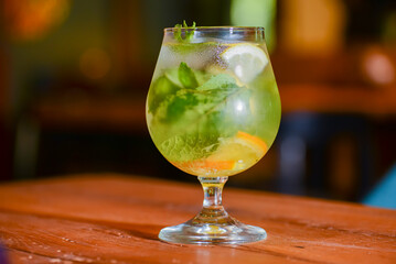 Classic fresh mojito on the table in a bar. Alcohol cocktail with ice, mint and lime on table with blurred background.