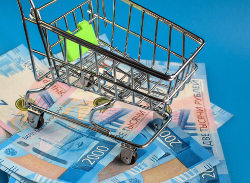 Russian Rubles Under The Basket On A Blue Background. Empty Grocery Cart On The Background Of 2000 Ruble Bills. View From Above. Selective Focus.