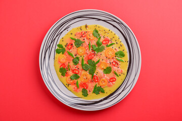Chilled cucumber avocado soup with salmon fish, tomato, pepper, fresh greenery served in a plate over red background.