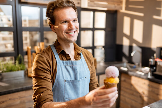Portrait of a cheerful ice cream seller in working uniform holding ice cream in waffle cone in the shop