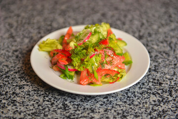 Vegetable salad with radishes,cucumber, sweet pepper and dill. Served in a white plate over grey textured table.