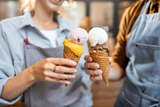 Two sellers cheering with yummy ice creams in waffle cone, having fun while selling ice cream at the shop, close-up