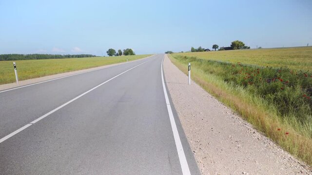 Winding asphalt road in Latvia. Along the edges sown fields of argo with cereals to the horizon. Red poppies on the sidelines. Baltic state