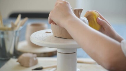 Close-up of potter making pot in pottery workshop. Using sponge and water for moisturizing clay.