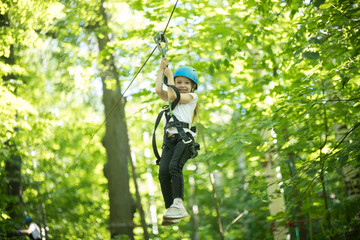 A little girl hanging on the insurance cable of her belt - rope bridge entertainment attraction
