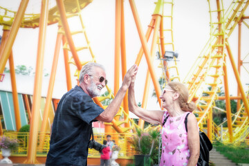 Obraz premium Elderly couple spending time together at theme park on summer weekend, senior people hanging out and having fun at an amusement park.